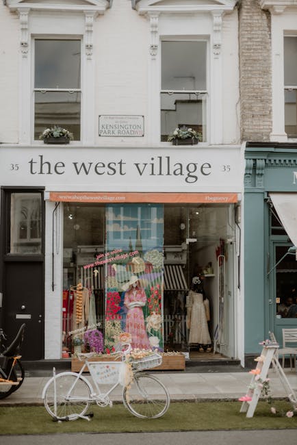 A floral display outside The West Village flower shop located on Kensington Park Road, featuring a mannequin dressed in a pink floral dress surrounded by vibrant flower arrangements. The shop window s