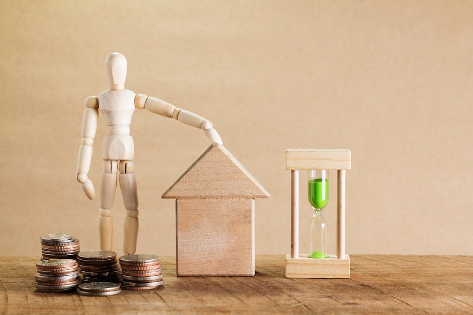 A wooden artist mannequin with articulated limbs leans on a small wooden house model, positioned on a wooden surface alongside neatly stacked coins, symbolizing costs. To the right, there is a small w